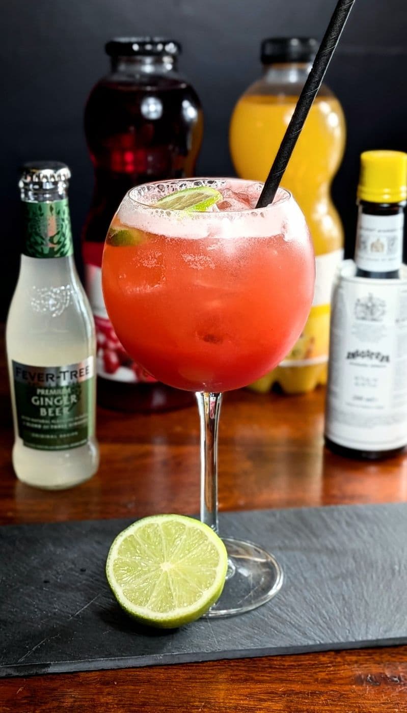 Cocktail rose au ginger beer dans un verre ballon, citron vert
