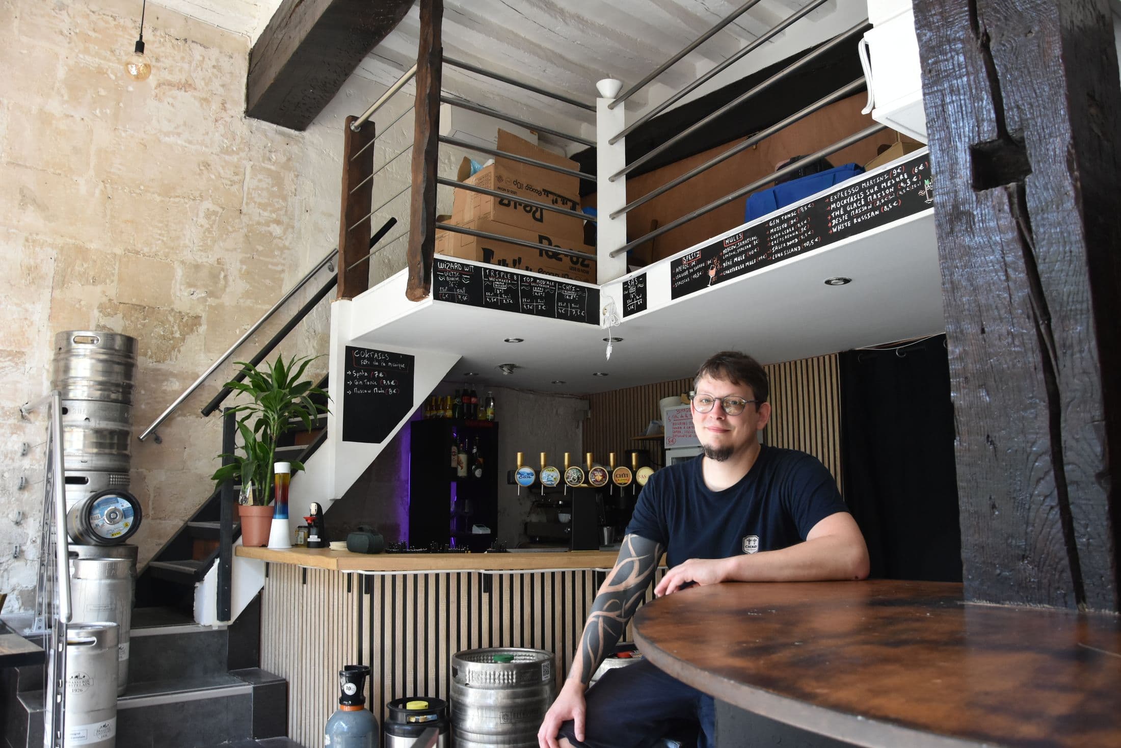 La salle du Bec : murs en pierre, escalier vers la mezzanine, fûts et comptoir aux cinq tireuses