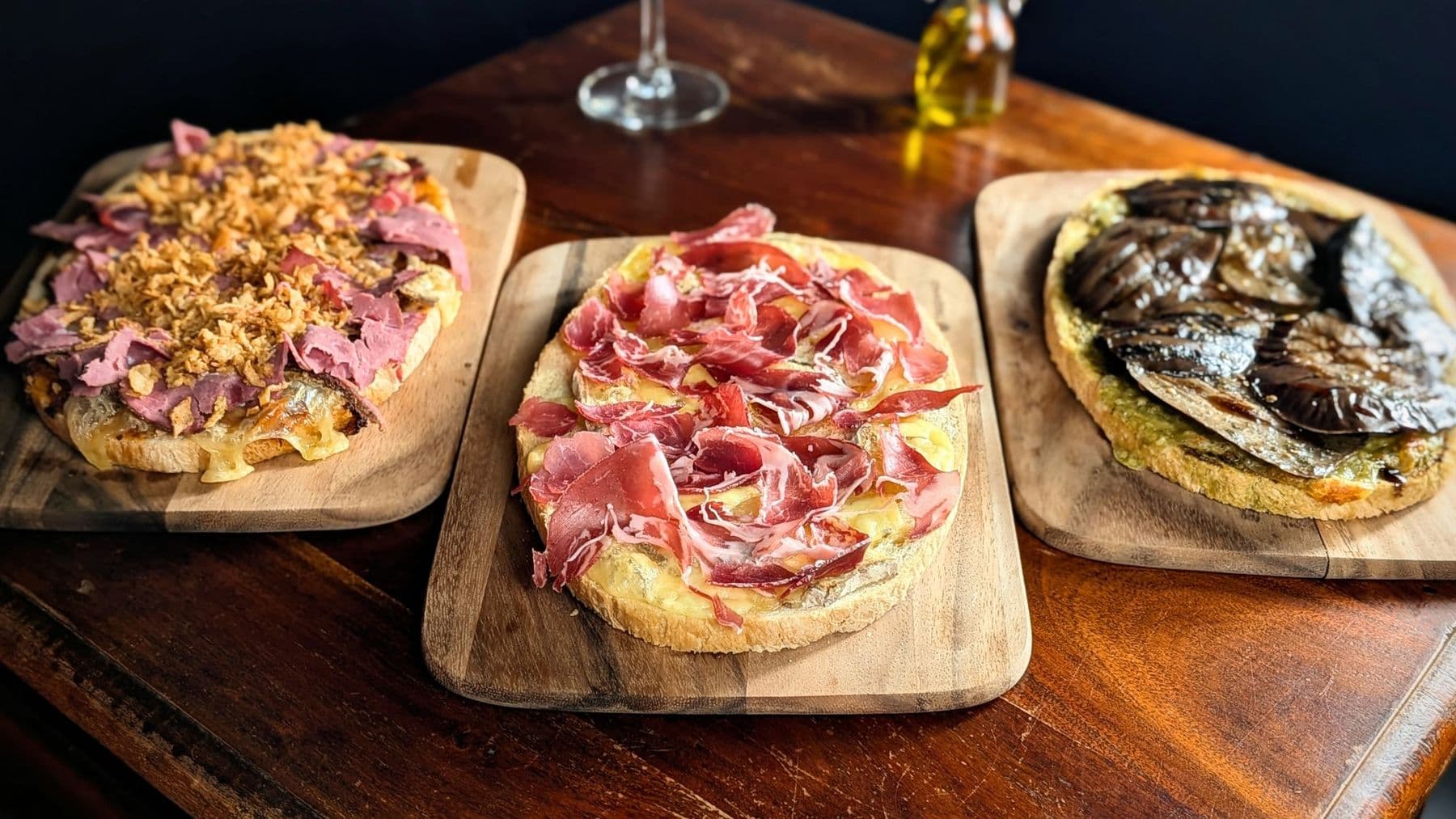 Trois tartines gratinées sur planches de bois : aubergine, jambon cru, pastrami