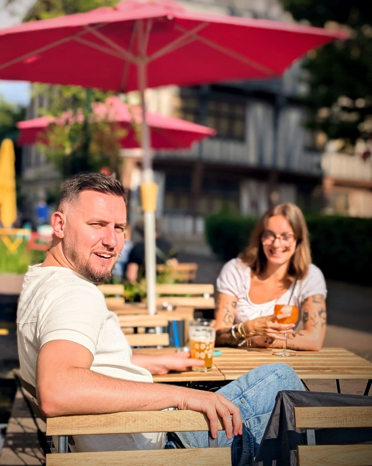 Deux clients sous les parasols rouges de la terrasse, maisons à colombages derrière