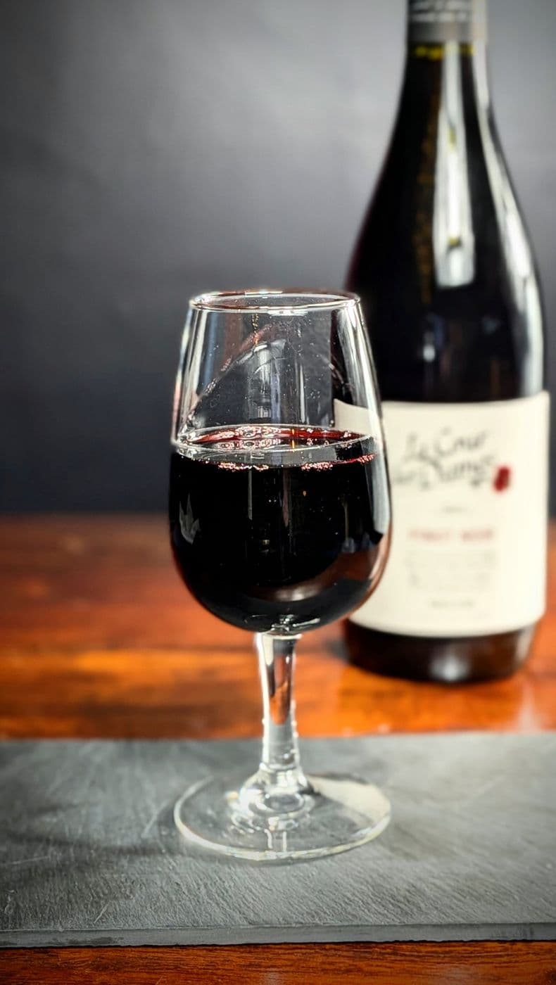 Verre de vin rouge devant une bouteille de pinot noir